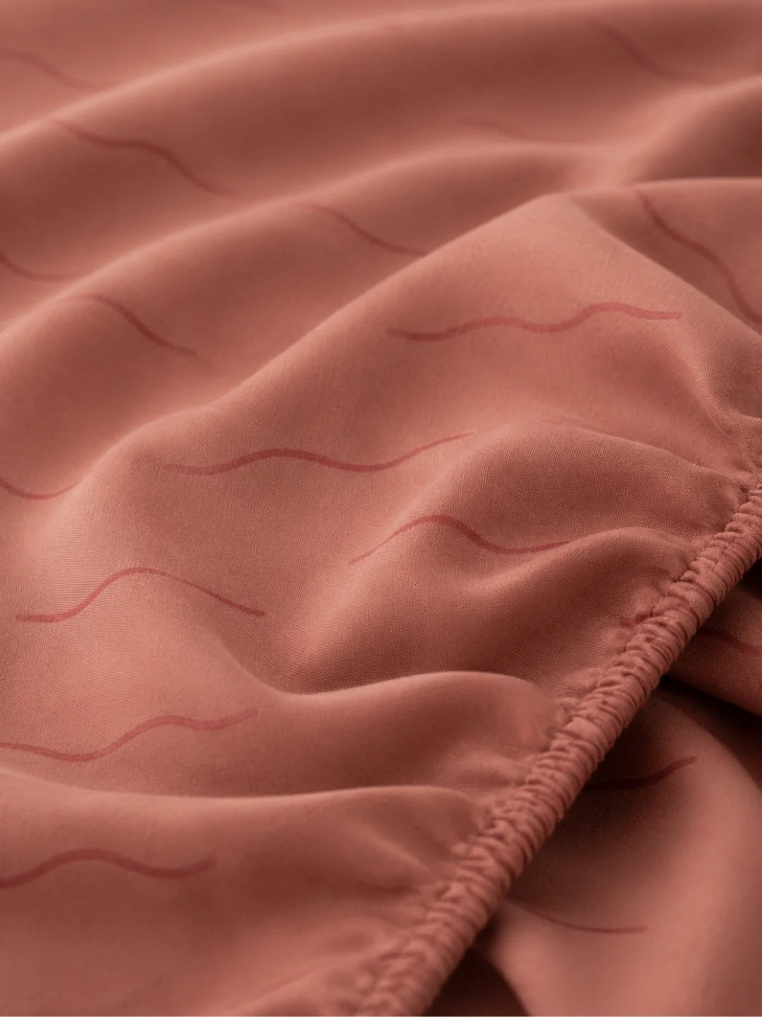 Close-up of a dusty rose pink fitted sheet with a subtle wavy pattern in organic cotton.