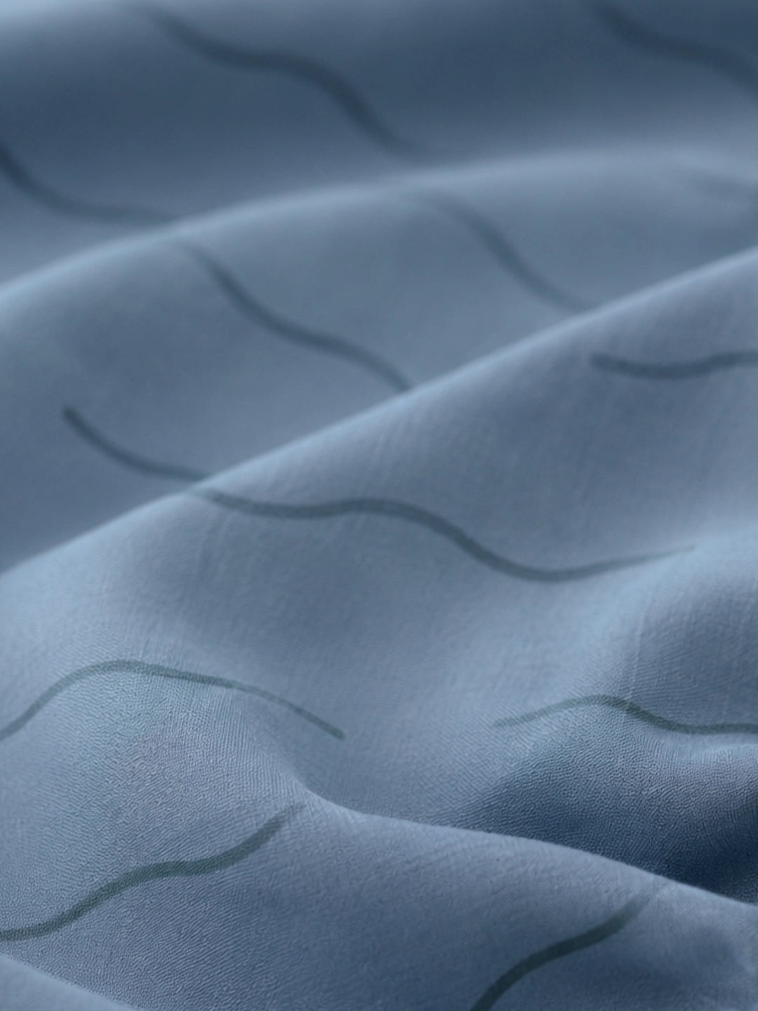 Close-up of a blue fitted sheet with a subtle wavy pattern in organic cotton.