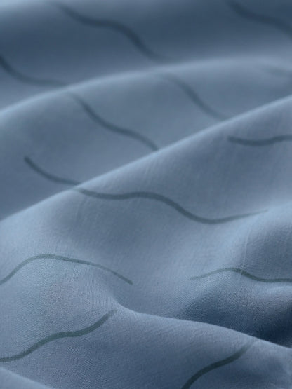 Close-up of a blue fitted sheet with a subtle wavy pattern in organic cotton.