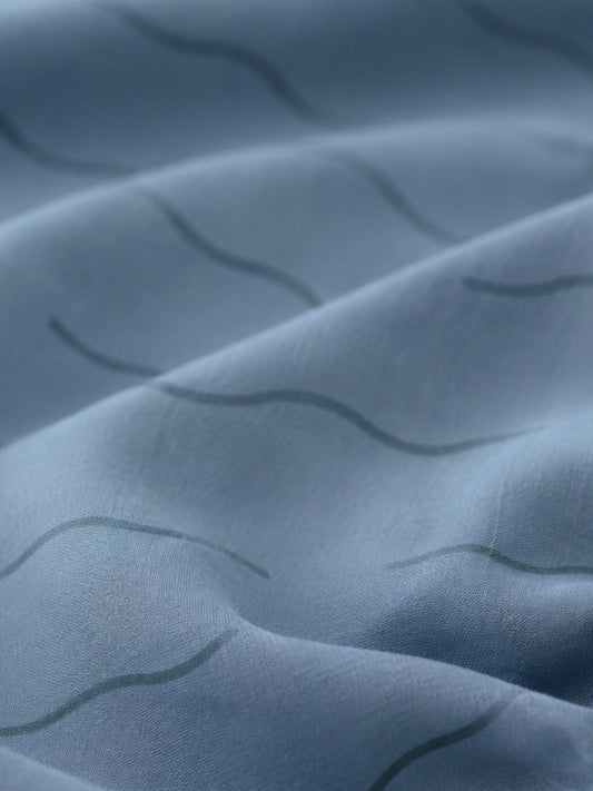Close-up of a blue fitted sheet with a subtle wavy pattern in organic cotton.
