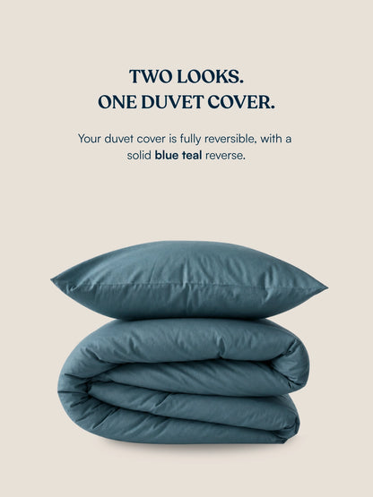 A folded duvet cover and matching pillow in a muted blue-teal color on a light beige background, with text above reading 'TWO LOOKS. ONE DUVET COVER.