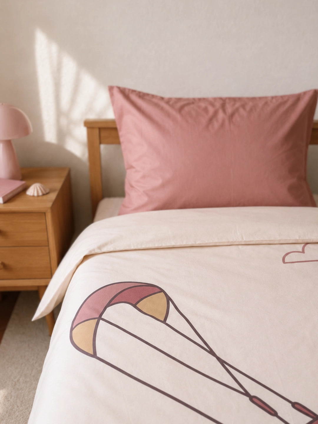 A styled bedroom scene showing a bed with a cream-colored and dusty pink duvet cover set for kids featuring an illustration of a girl Kitesurfer.