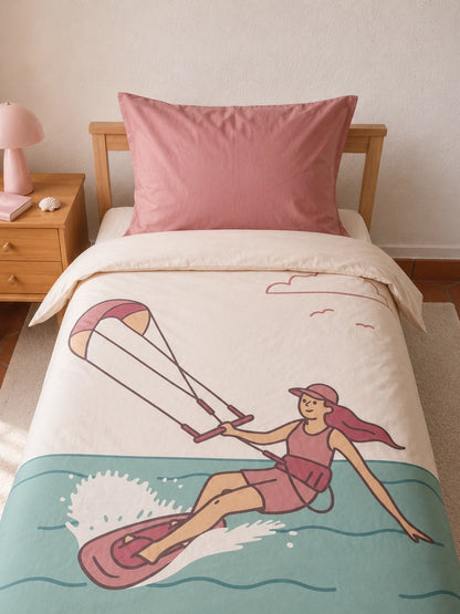 A single bed dressed in an off white organic cotton bedding set for kids with an illustrated print of a girl Kitesurfing across teal water, styled with a dusty pink pillowcase in a warm, minimalist bedroom.