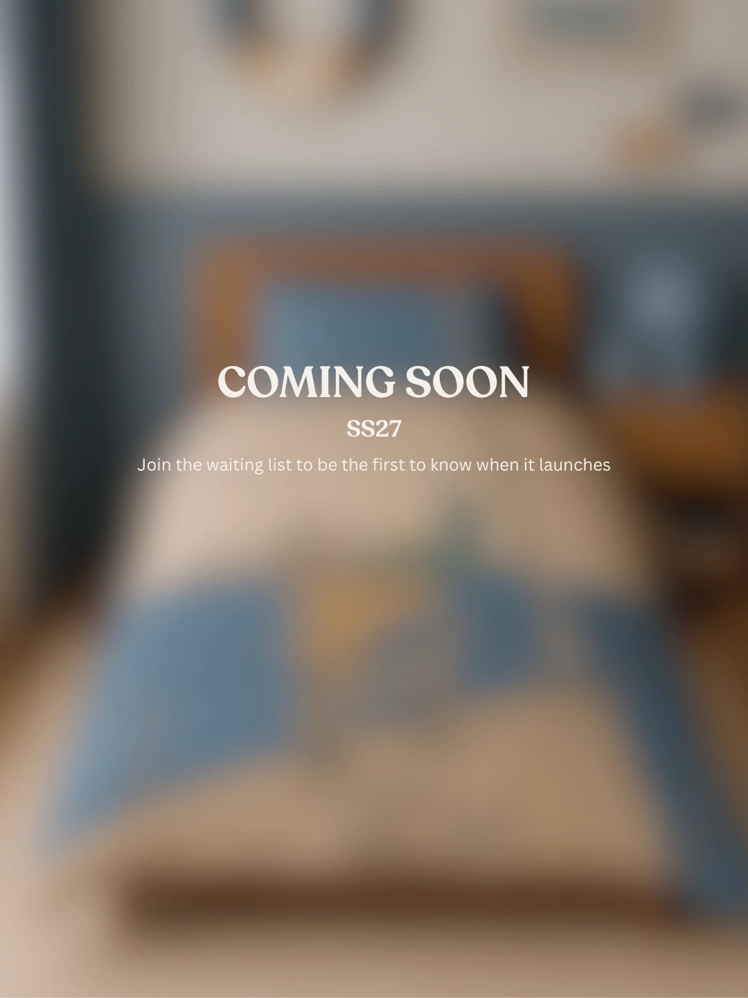 A blurred bedroom scene with a bed and bedding in soft blue and beige tones, overlaid with the text 'COMING SOON SS27' and smaller text below inviting people to join the waiting list.