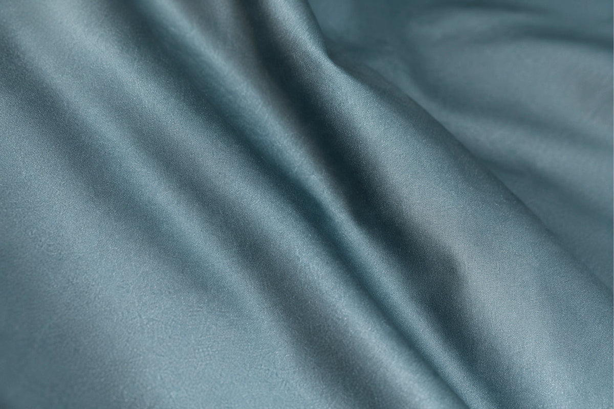 A close-up of draped organic cotton duvet cover set for kids in a dusty slate blue color, showing soft folds and a subtle sheen.