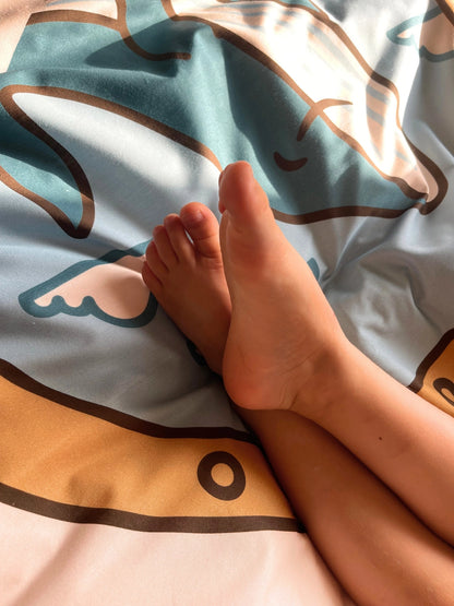 A close-up of a toddlers bare feet resting on a light blue and beige patterned duvet cover set. 