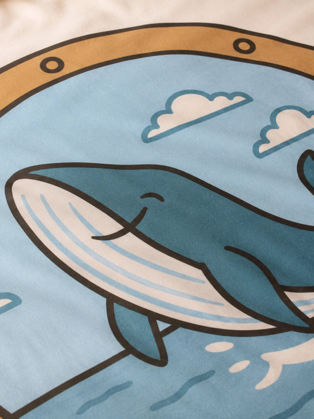 A close-up of a duvet cover set for kids featuring a cartoon whale illustration with white clouds in a porthole.