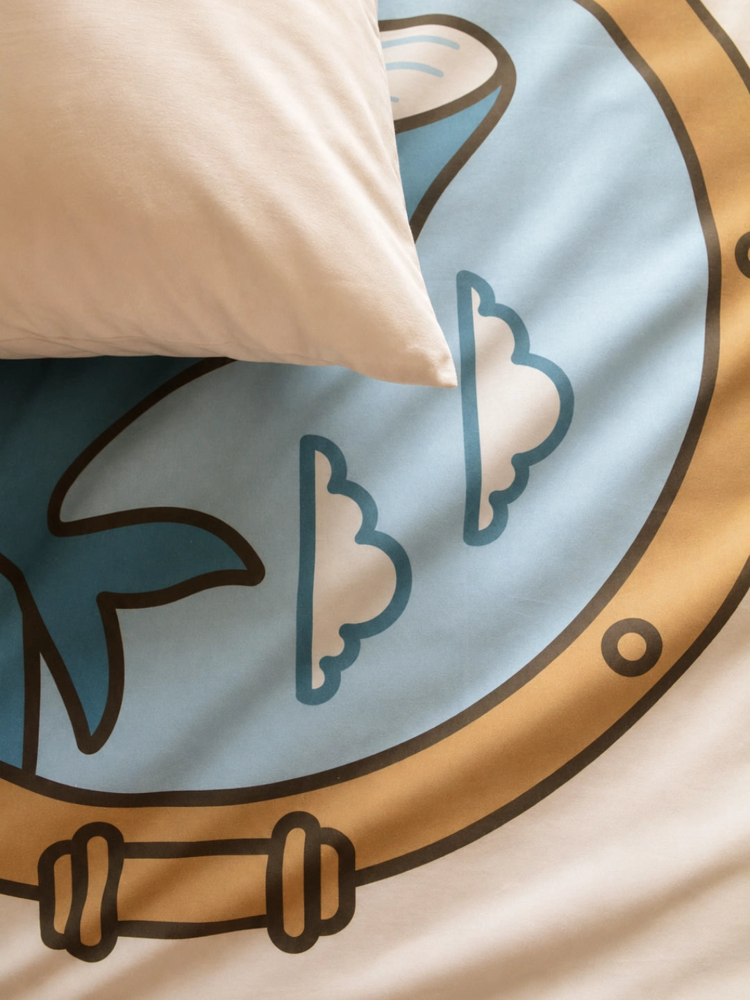 A close-up of a organic duvet cover set featuring a porthole graphic with a whale inside, with a cream-colored pillow resting on top.