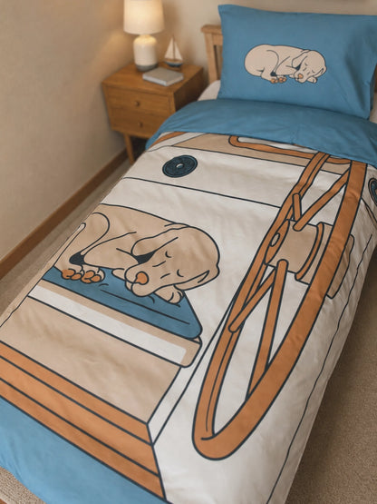 A single bed in a bedroom styled with a illustration duvet cover and matching pillowcase featuring a sleeping dog on a sailboat.