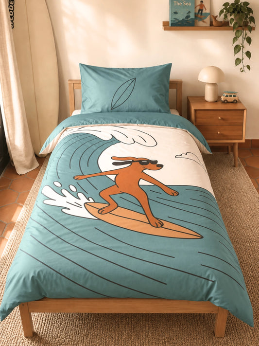 A single bed dressed in a teal and white surf-themed bedding set, featuring a cartoon dog surfing on a wave. The room setting includes a wooden nightstand, a lamp, a shelf with a book, and a hanging plant.